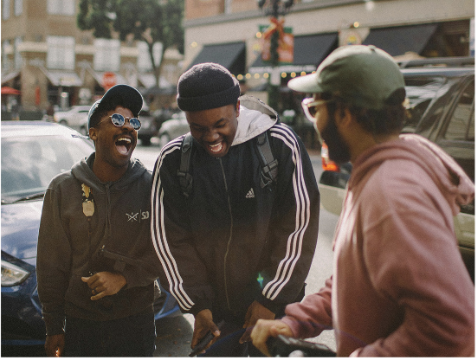 three men, all wearing ball caps, stand together laughing